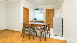 A dining area with a wooden table and chairs, a refrigerator, and a kitchen in the background. - Sakura Hotel (Yangon)