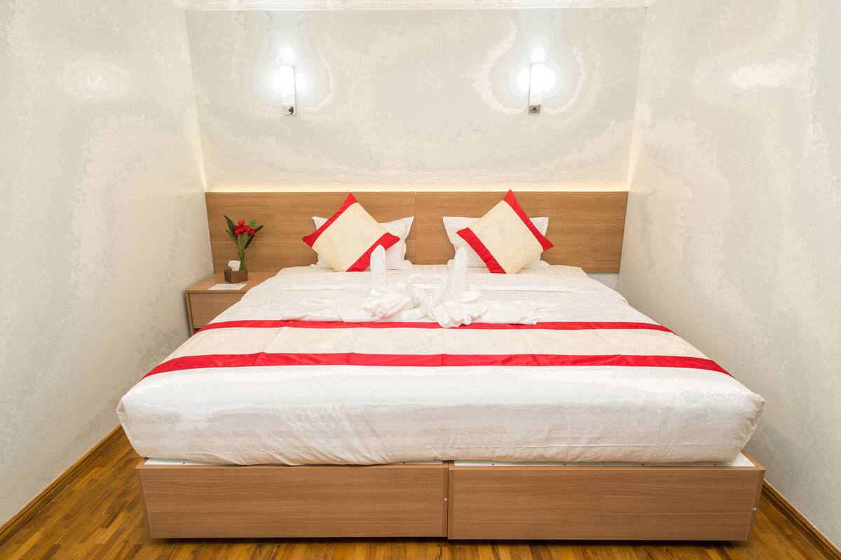 A neatly made bed with a wooden headboard, white bedding, and red accents.