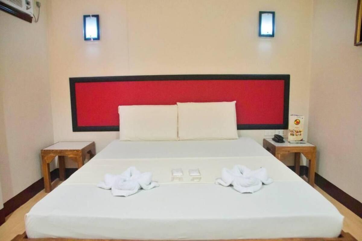 A hotel room with a large bed, two bedside tables, and a red headboard.