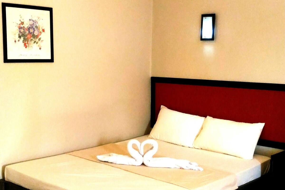 A neatly made bed with a red headboard, a framed picture on the wall, and a small bedside table.