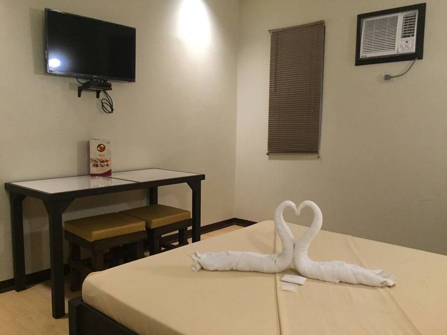 A hotel room with a bed, a desk, a television, and a window with blinds.