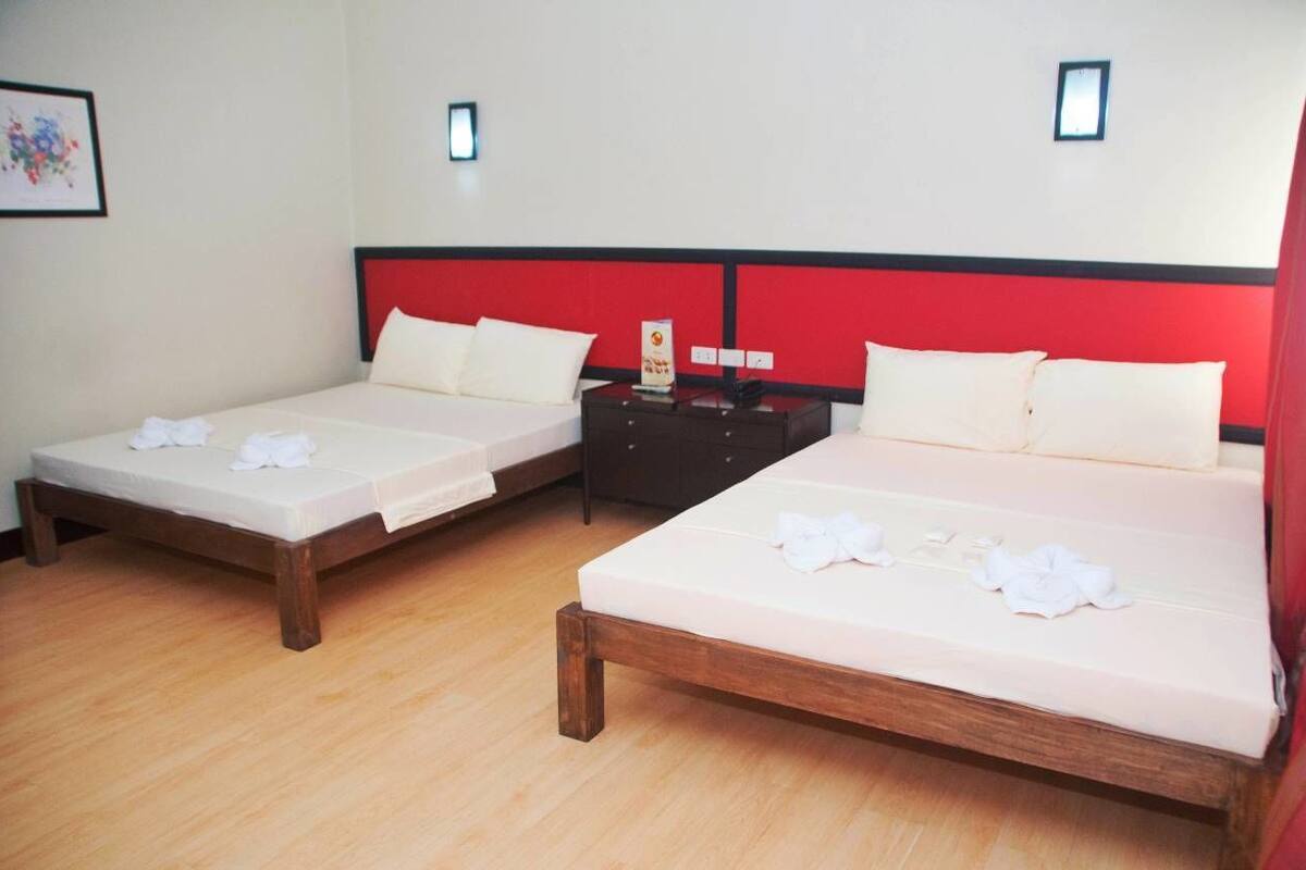 Two single beds with wooden frames and white bedding, a nightstand with a lamp, and a red headboard.
