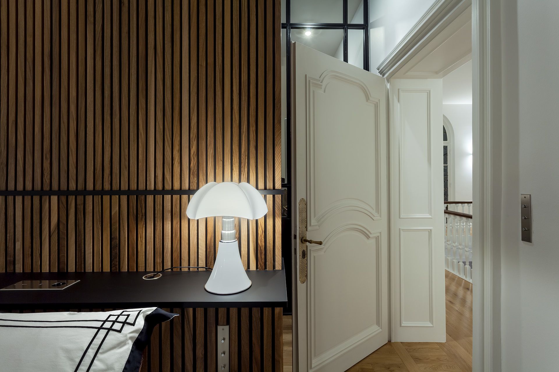 Een moderne kamer met een wand van houten latten, een witte deur en een tafel met een lamp.