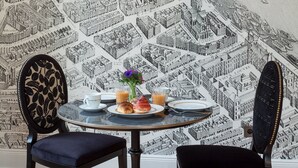 A dining area with a round table, two chairs, and a wall mural of a cityscape. - Villa Camoufle (Metz)