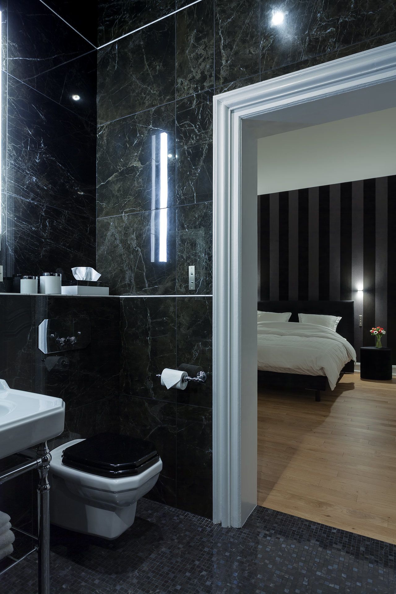 A modern bathroom with a black marble sink, toilet, and shower. A white toilet paper holder is visible.