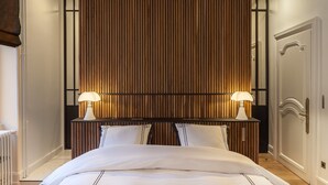 A hotel room with a large bed, two bedside lamps, a wooden panel headboard, and a classic door. - Villa Camoufle (Metz)
