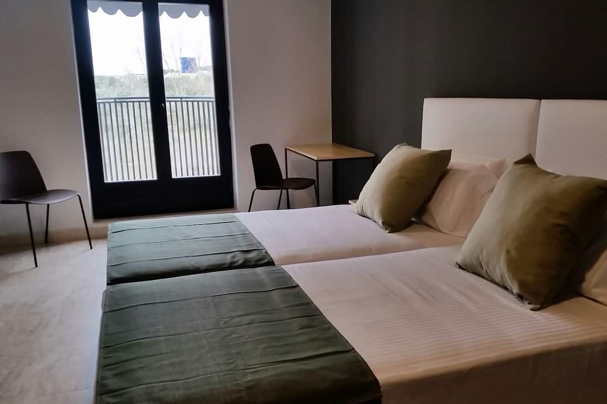Een hotelkamer met een bed, twee stoelen, een tafeltje en een balkon met een hekwerk.