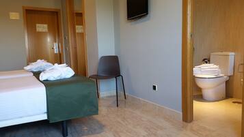 Habitació d'hotel amb llit, una cadira, un vàter i una televisió penjada a la paret.