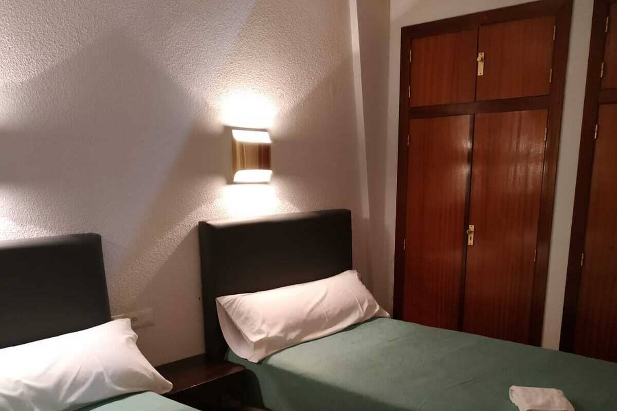 Een hotelkamer met twee eenpersoonsbedden, een nachtkastje, een wandlamp en een houten garderobe.