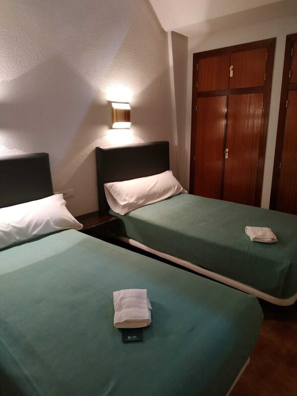 A hotel room with two single beds, a nightstand, a wall-mounted lamp, and a wooden wardrobe. - Balneario de Ledesma (Vega de Tirados)
