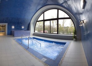 An indoor swimming pool with a view of trees through a large arched window. - Balneario de Ledesma (Vega de Tirados)