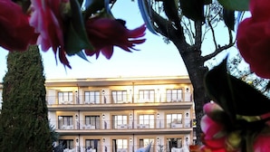 A multi-story hotel with balconies, a well-maintained garden, and a paved driveway.