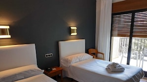 A hotel room with two single beds, a nightstand, a chair, and a window with blinds.