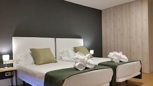 A hotel room with two beds, each with a green pillow and white linens. There are towels and a robe on each bed.