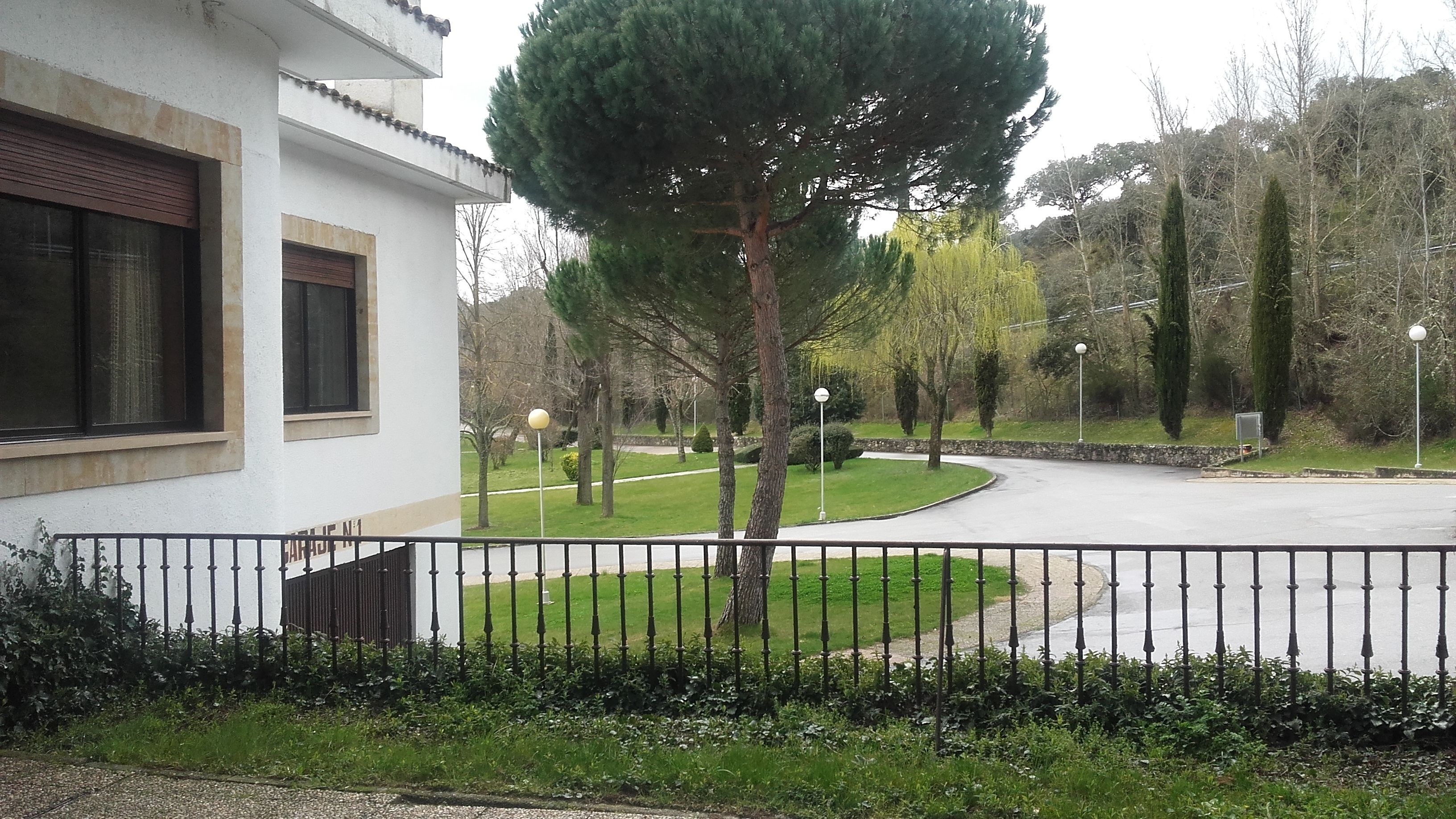 Un edificio con fachada blanca, cerca de metal negro y un césped cuidado con árboles.