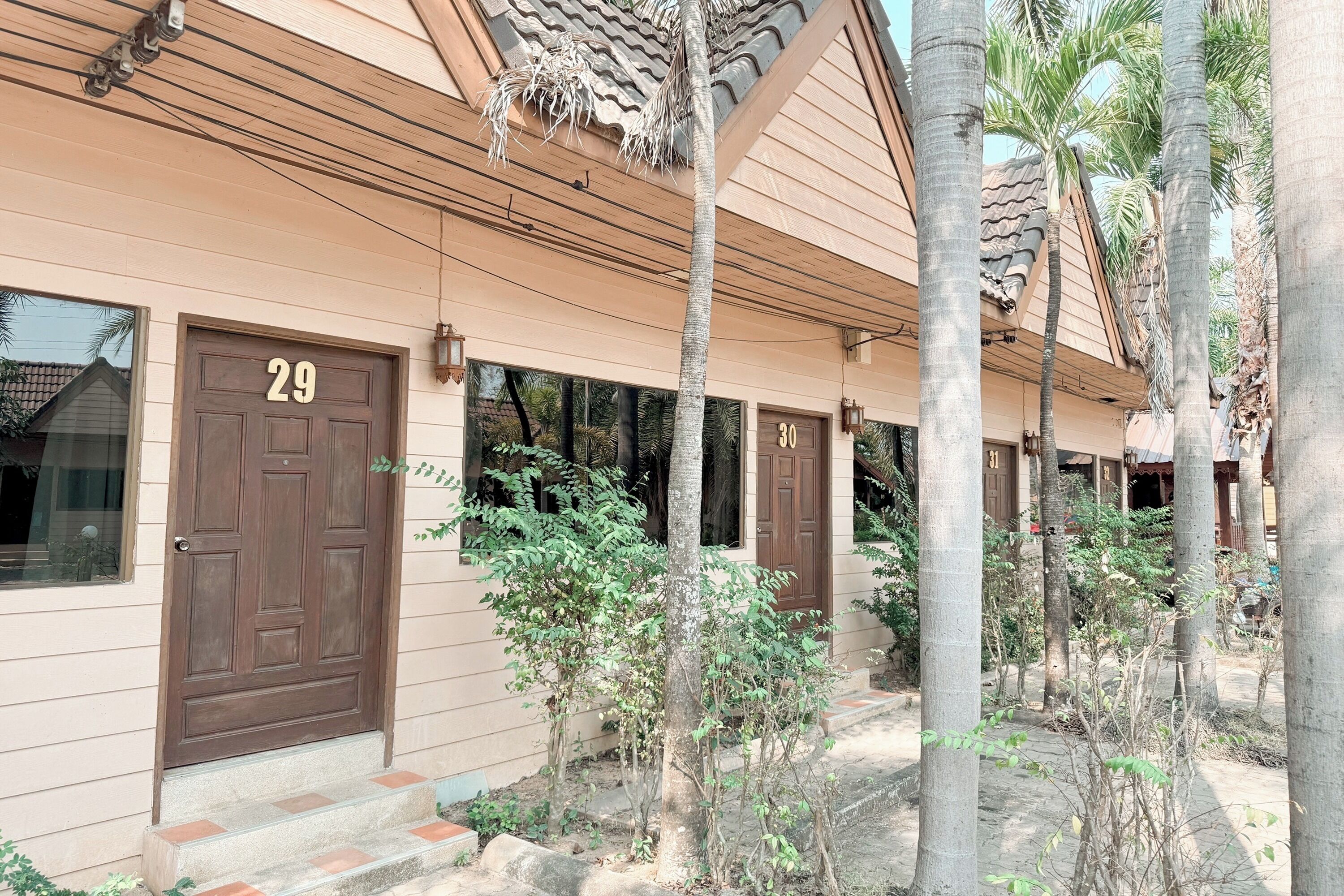 A building with numbered doors, likely a hotel or guesthouse, with a tiled roof and palm trees in the vicinity.