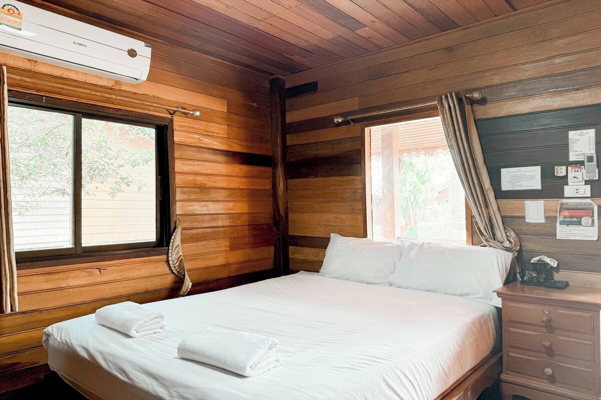 A wooden-paneled room with a bed, a nightstand, and a window with curtains.
