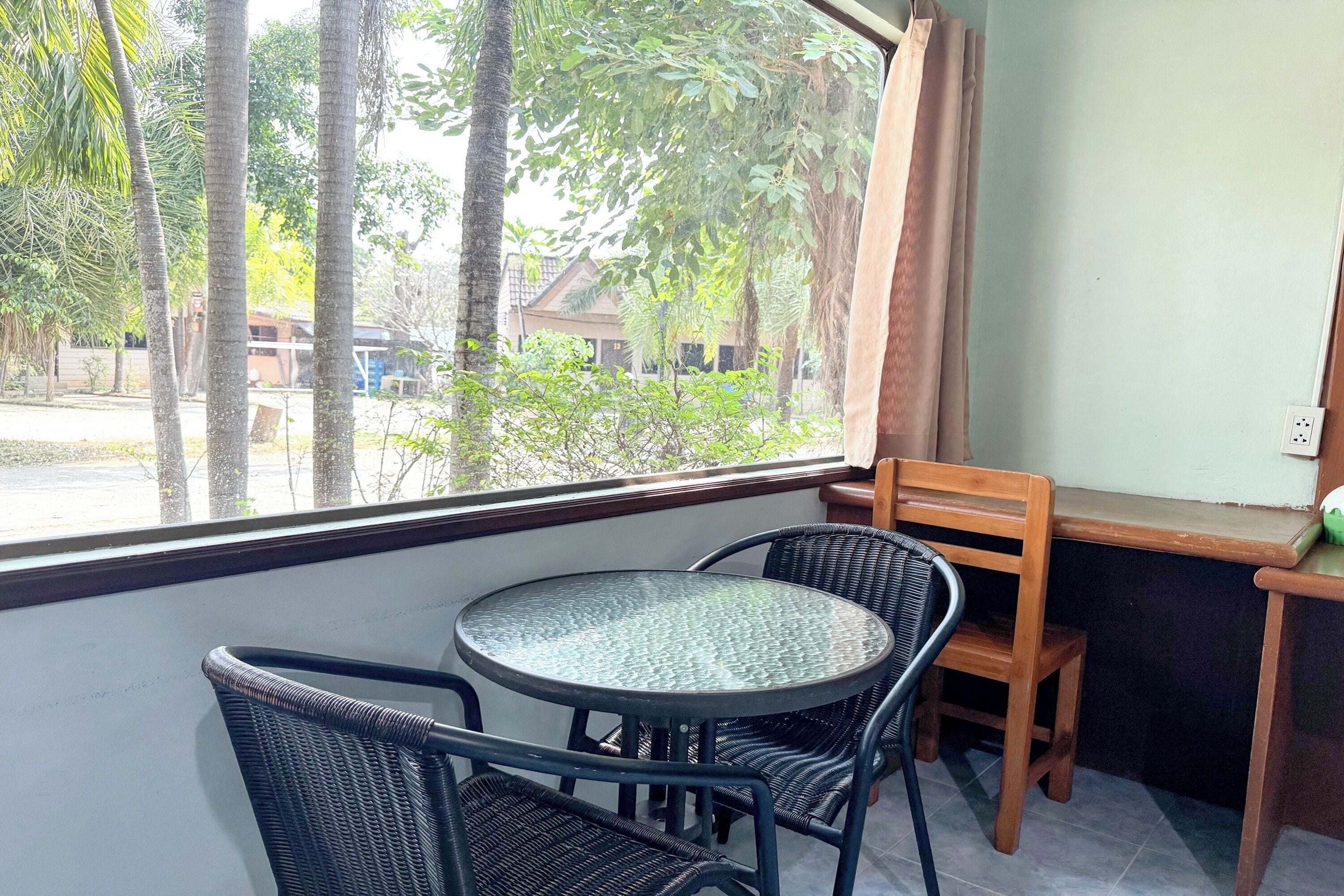 A small round table with four wicker chairs, a window with curtains, and a view of trees and buildings outside.