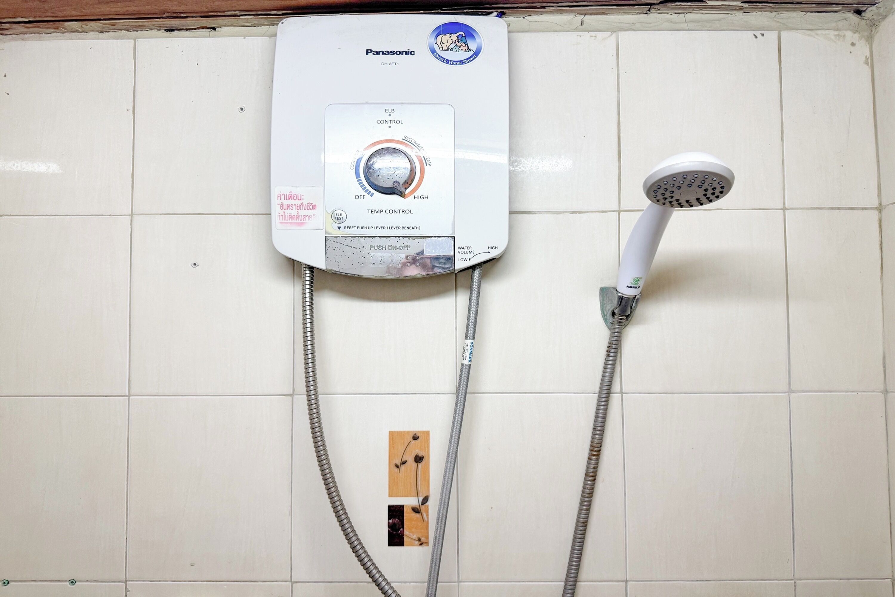 Ducha eléctrica Panasonic montada en la pared, con panel de control, dos mangueras flexibles y un cabezal de ducha.