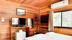 A wooden cabin room with a bed, a television, a small refrigerator, and a window with curtains. - The Northern View Hotel (Sung Men)