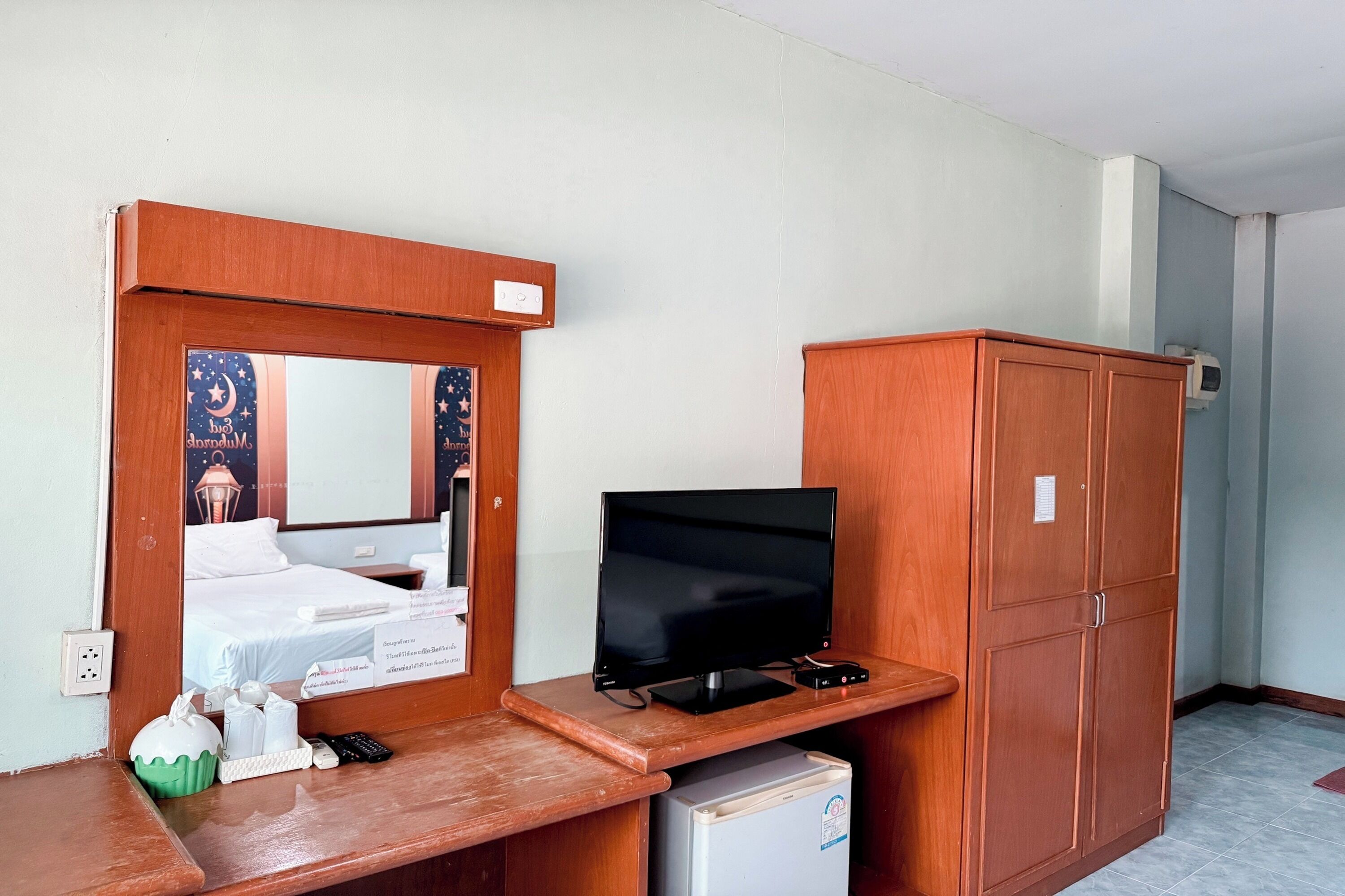 A hotel room with a wooden desk, a television, a wardrobe, and a bed with a night sky-themed headboard.