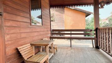 A wooden porch with a bench and table, a view of a building in the background, and a railing with decorative elements.