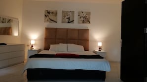 A modern bedroom with a large bed, bedside tables with lamps, a dresser, and three wall-mounted paintings. - Yamsafer Homes 4th Circle (Amman)