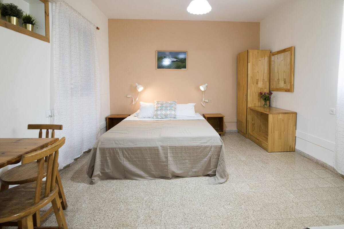 Un dormitorio con cama, mesitas de noche, un armario de madera, un escritorio y una silla.