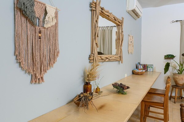 A room with a long wooden table, a macrame wall hanging, and a rustic mirror.