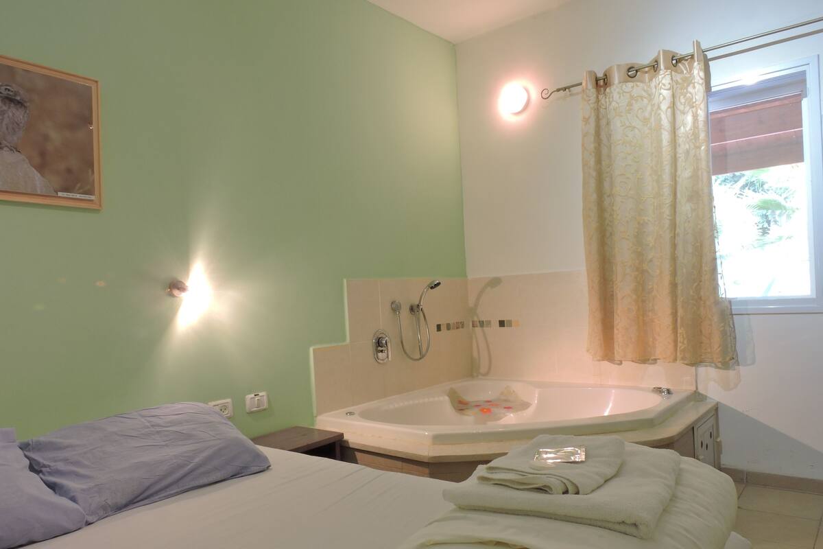 Un dormitorio con cama, un baño con lavamanos y ducha, y una ventana con cortinas.