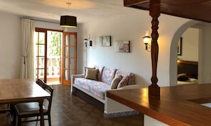 Un comedor con una mesa y sillas de madera, un sofá con cojines estampados y un trave de madera en el techo.