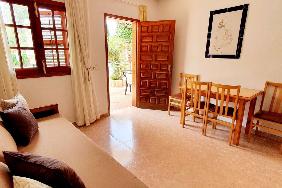 Une pièce comprenant un canapé, une table à manger avec des chaises, une porte en bois et une fenêtre avec des rideaux.
