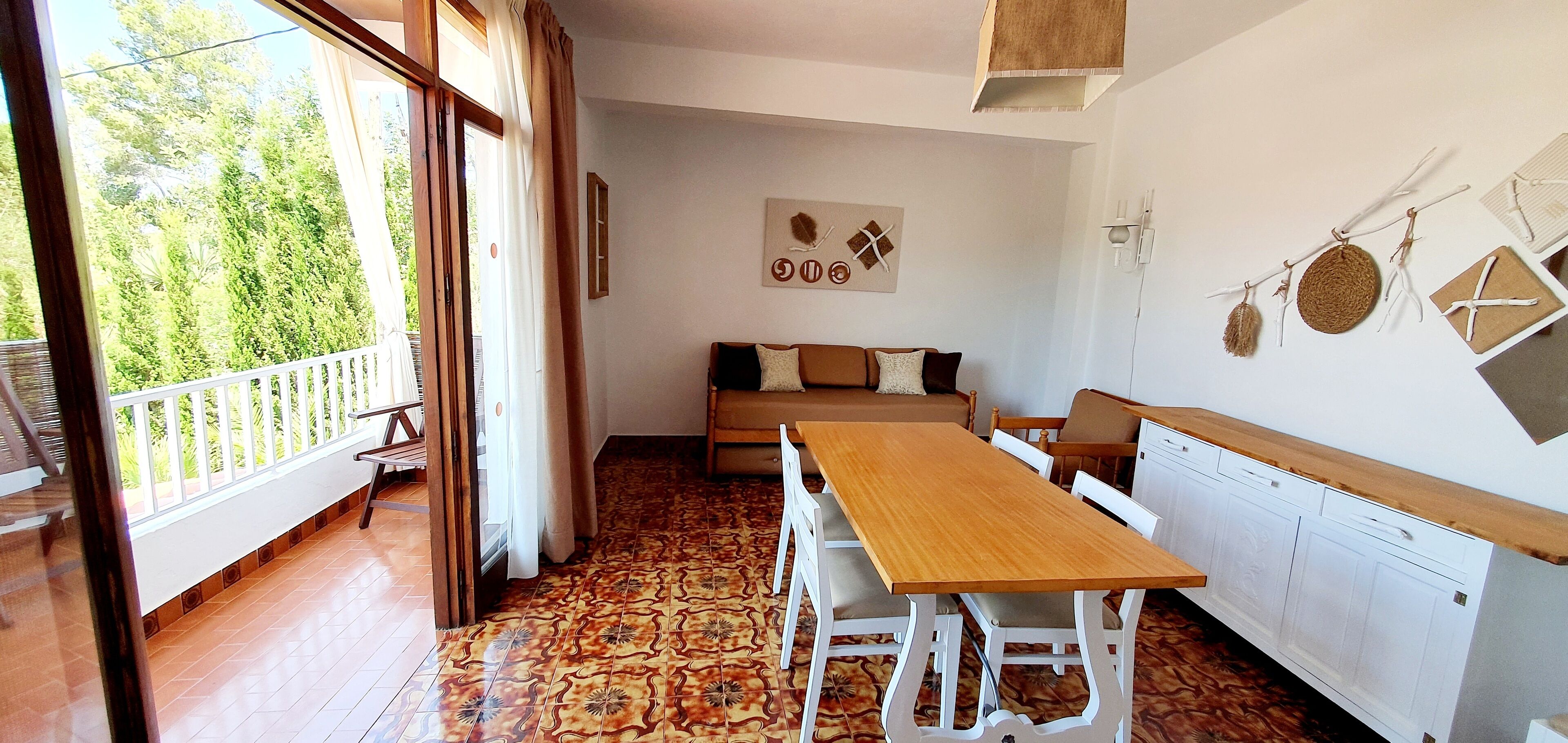 Una habitación con una mesa y sillas de madera, un sofá y un balcón con vistas a zonas verdes.