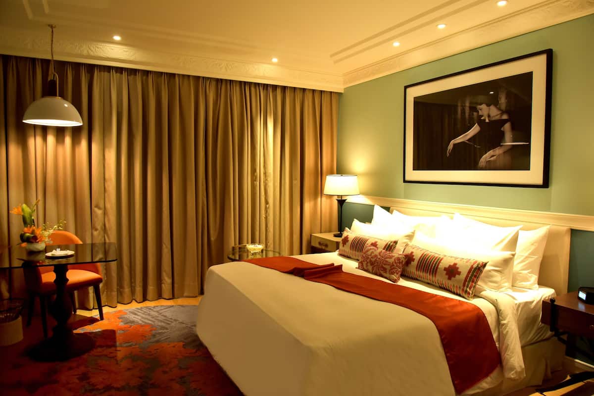 A hotel room with a bed, a desk with a lamp, a framed picture on the wall, and a curtain.