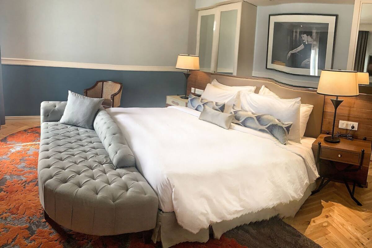 A bedroom with a large bed, a sofa, two nightstands, a lamp, and a mirror.