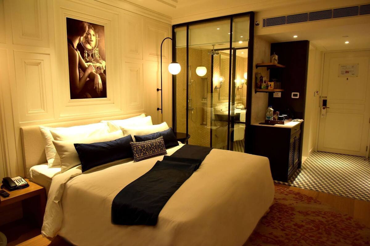 A hotel room with a large bed, a glass-enclosed shower, a small desk, and a mirror.