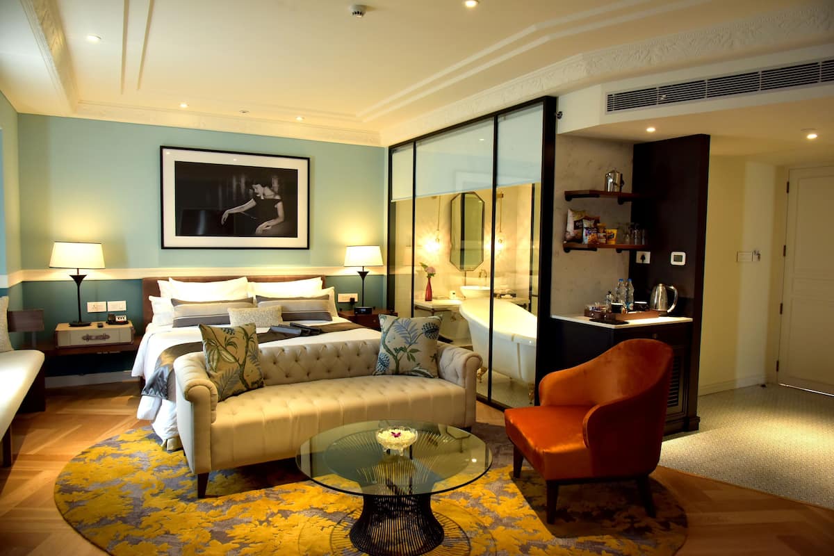 A hotel room with a bed, a sofa, a glass coffee table, a chair, a desk, and a mirror.