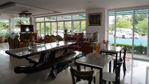 Un vaste espace dédié à la salle à manger, avec une grande table et des chaises en bois, un téléviseur et une vue sur le parking grâce à de grandes fenêtres.