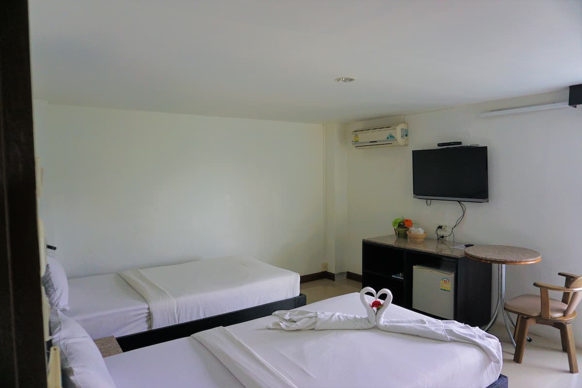 Una habitación de hotel con dos camas individuales, un escritorio con silla, un televisor y un refrigerador pequeño.