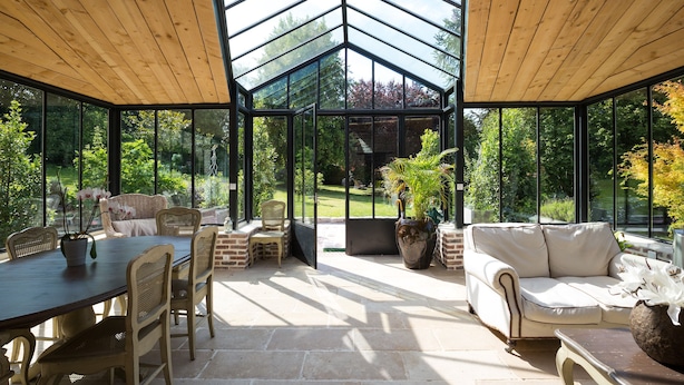 Una veranda con soffitto in legno, un tavolo da pranzo con sedie, un divano e piante in vaso.