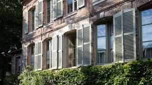 Un edificio a due piani con facciata in mattoni, persiane verdi e un ingresso coperto con una porta.