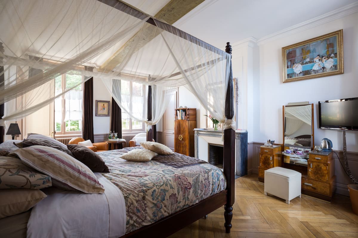 A bedroom with a four-poster bed, a canopy, a television, and a fireplace.