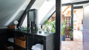 Un bagno moderno con una parete rivestita in piastrelle nere, un lavabo a forma di coppa in vetro, cesti in vimini e uno specchio.