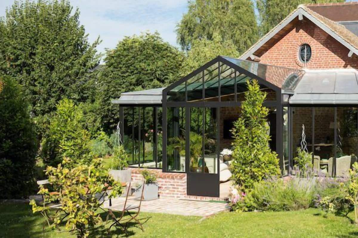 A house with a glass conservatory, brick walls, and a garden.