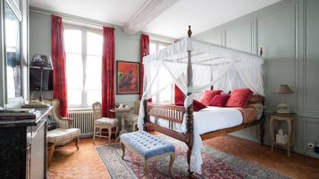 Ein Schlafzimmer mit Himmelbett, einer Sitzecke mit Bank, einem kleinen Tisch und einem Heizkörper.