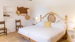 A bedroom with a wooden bed, a nightstand with a lamp, a chair, and a shelf with a hat. - Son Sant Andreu (Petra)