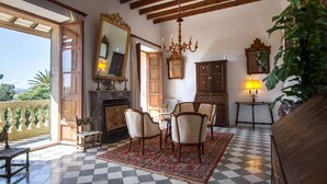 A spacious room with a checkered floor, a fireplace, a dining table with chairs, a chandelier, and a large mirror. - Son Sant Andreu (Petra)