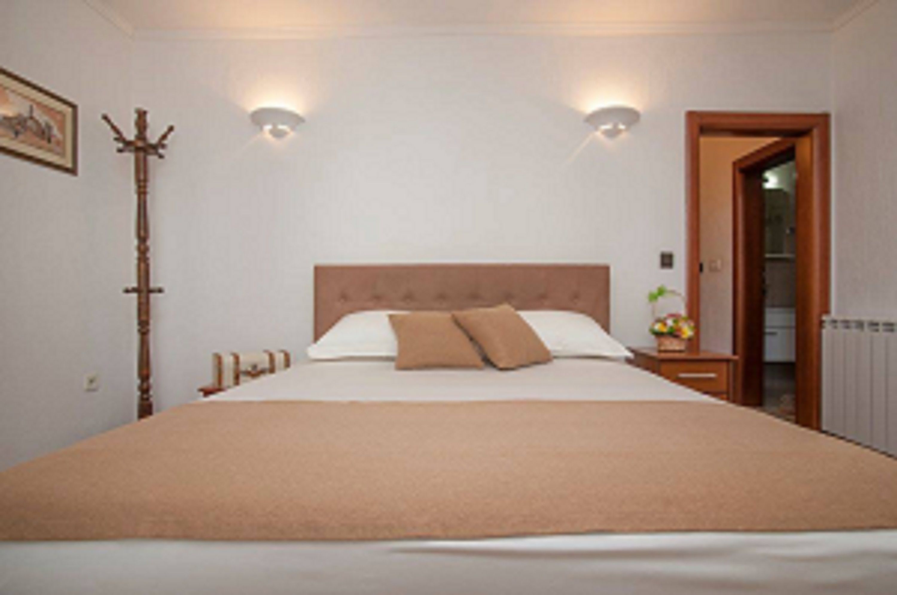 A neatly arranged bedroom with a large bed, a bedside table with a lamp, and a coat rack.