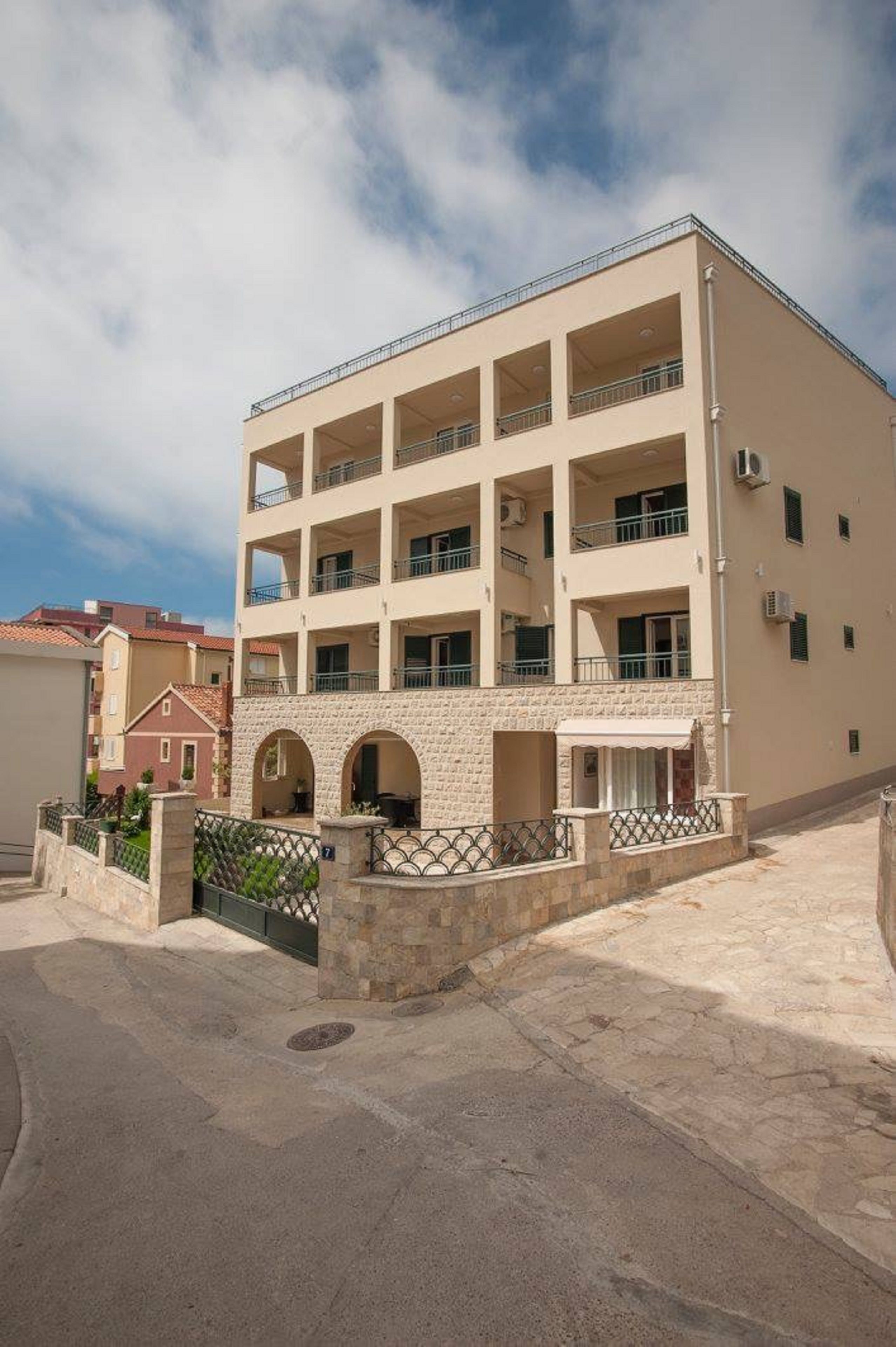 A multi-story building with balconies, a stone entrance, and a paved courtyard.