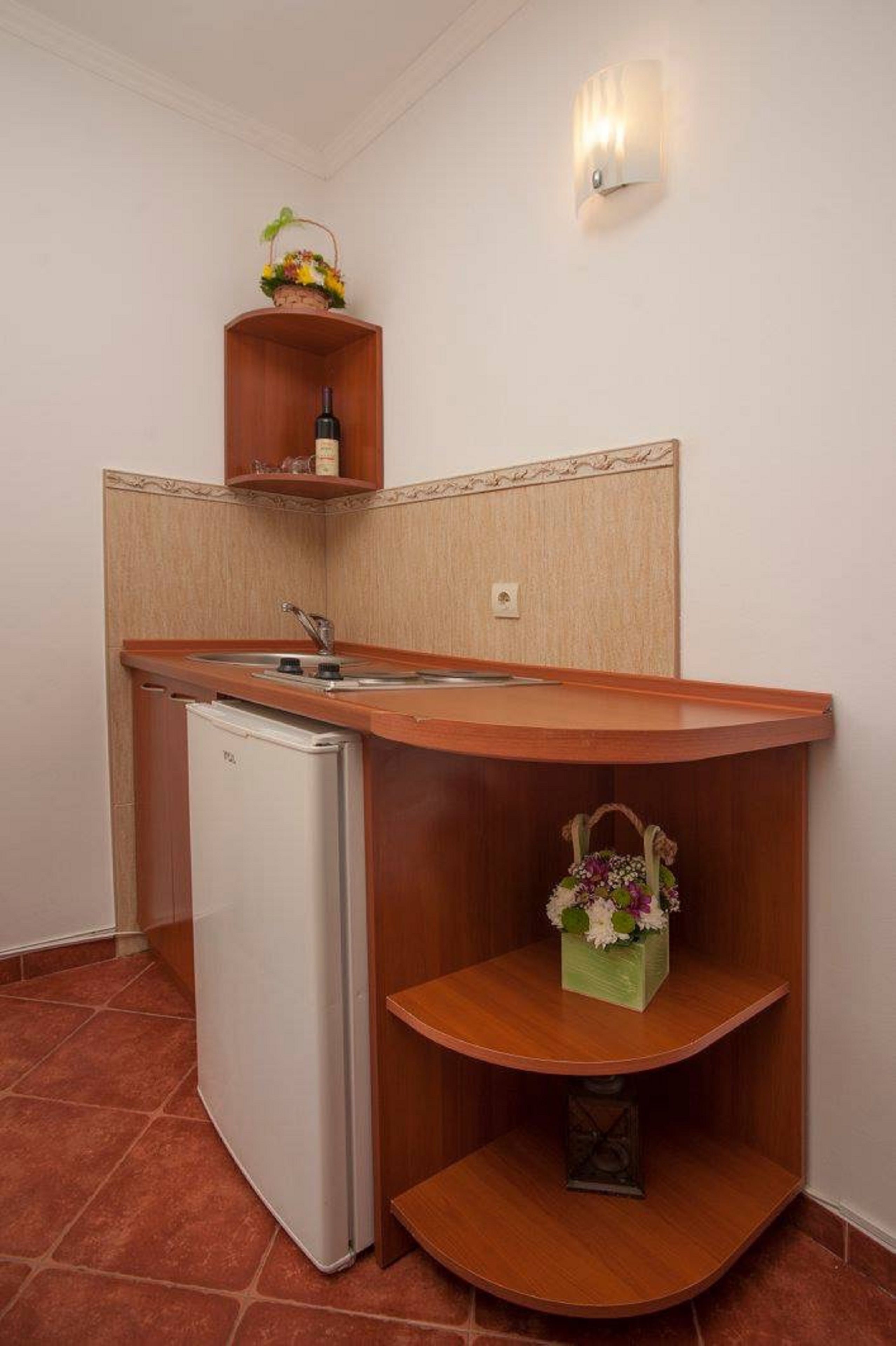 Une cuisine compacte avec un réfrigérateur blanc, un plan de travail en bois, un évier et une petite étagère sur laquelle se trouve un panier de fleurs.